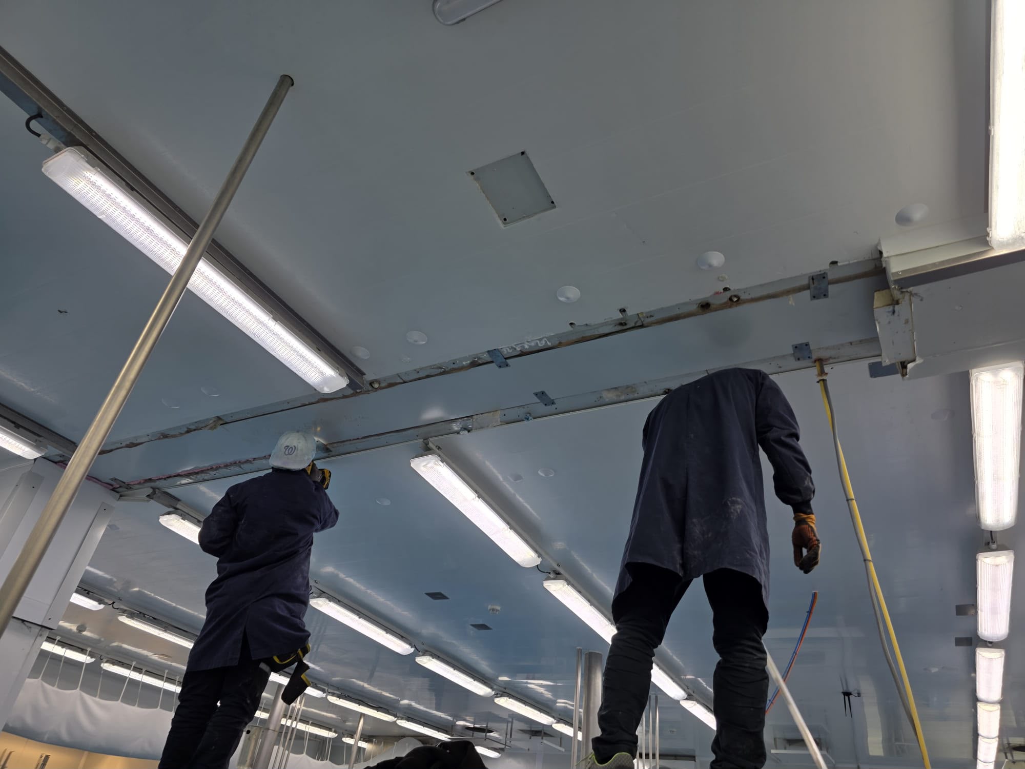 Dos operaris de Trívium muntant el sostre d'una sala blanca